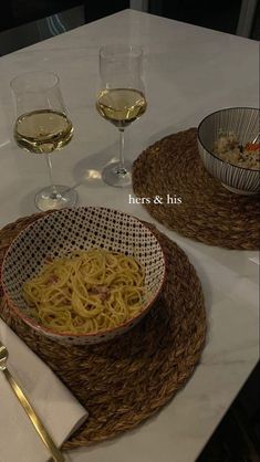 two glasses of wine are sitting on a table with some food and pasta in bowls