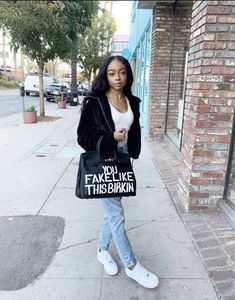 a woman is standing on the sidewalk holding a bag