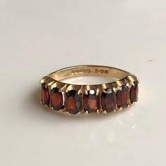 A vintage 9 carat yellow gold stone garnet ring. The setting holds the seven cut stones beautifully letting them glow! CONDITION: Good condition, wear consistent with age and use. Please see photos for more detail. HALLMARKED 9 CARAT GOLD, ASSAYED IN BIRMINGHAM 1975 BAND WIDTH: 2mm GARNET DIAMETER: 5mm x 3mm (.15 carats) SETTING LENGTH: 25mm  RING SIZE: UK: M 1/2 | US: 6 1/2 WEIGHT: 3.1g  (UZZ) Garnet Band Ring, Garnet Rings Vintage, Vintage Faceted Yellow Gold Rings, Vintage Faceted Rings For Anniversary, Infinite Jewelry, Vintage Garnet Rings, 1975 Band, Garnet Ring Gold, Gold Garnet Ring