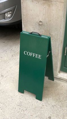 a green sign sitting on the sidewalk next to a car