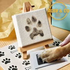 a dog paw prints on a canvas next to a small easel with a cat's paw in it