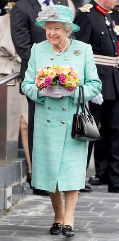 the queen is walking down the street with flowers in her hand