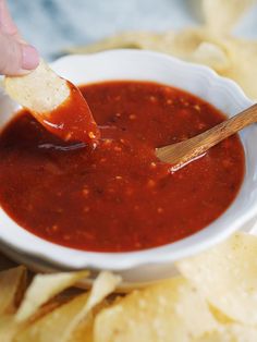 a person dipping tortilla chips into a bowl of chili sauce with a wooden spoon