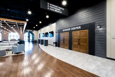 the inside of a building with wood flooring and black walls, white couches and wooden doors