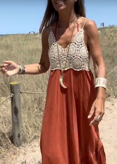 a woman standing on top of a sandy beach next to a wooden fence and grass