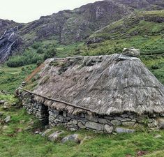 an old thatched roof house in the middle of a grassy area with mountains in the background