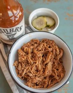 a white bowl filled with pulled pork next to a bottle of bbq