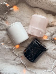 three cups sitting on top of a white blanket next to some lights and a teddy bear