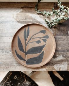 two plates with leaves painted on them sitting on a table next to some flowers and plants