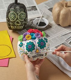 a person holding a paintbrush in front of a painted skull with flowers on it