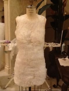 a mannequin made out of white yarn sitting on a table next to a plant