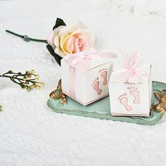 two small boxes with baby's footprints on them and a pink rose in the background