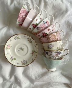 tea cups and saucers are lined up on a white sheet with pink flowers in them