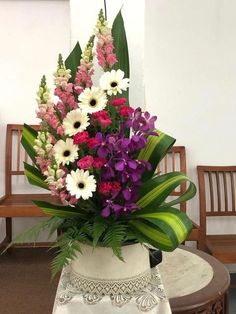 a white vase filled with lots of purple and white flowers next to a wooden bench