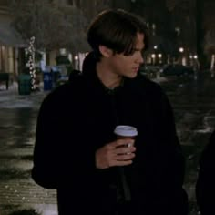 two young men standing next to each other on a street at night, one holding a coffee cup in his hand