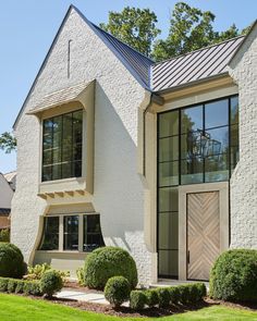 a white brick house with large windows and green grass in the front yard, on a sunny day