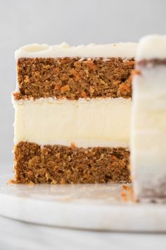 a slice of carrot cake with cream cheese frosting on a white marble platter