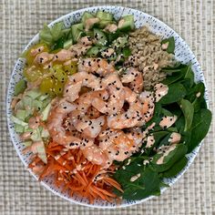 a white bowl filled with shrimp, carrots and spinach sprinkled with sesame seeds