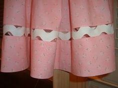 a pink curtain with white trim hanging from it's side in front of a window