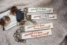 four keychains with different sayings on them sitting on a blanket next to sunglasses