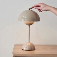 a person's hand reaching for an object on top of a wooden table next to a lamp