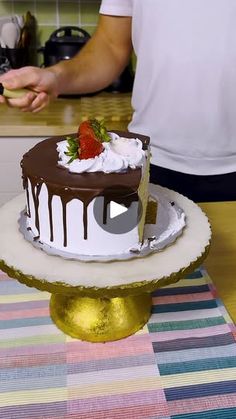 a man is cutting into a cake with chocolate and strawberries on top, while another person holds a knife in the background