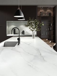 a large kitchen with marble counter tops and black pendant lights hanging from the ceiling over the sink