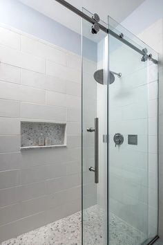 a walk in shower sitting next to a white tiled wall and counter top with shelves on each side