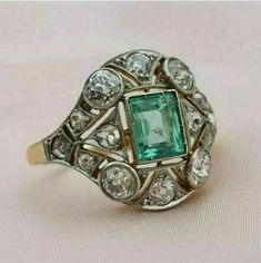 an antique emerald and diamond ring on a white surface with the center stone surrounded by smaller diamonds