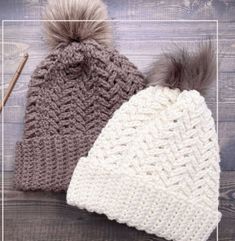 two knitted hats with pom - poms sitting on top of a wooden table