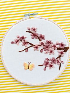 a white embroidery hoop with pink flowers and a yellow butterfly on it, sitting on a striped tablecloth