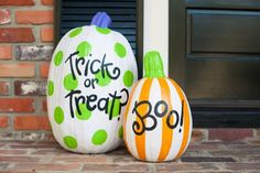 two painted pumpkins sitting next to each other in front of a brick building with the words trick or treat on them