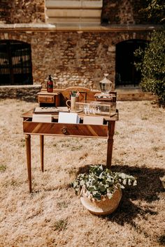 a wooden table sitting on top of a dry grass field next to a brick building