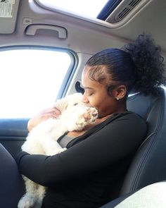 a woman sitting in the back seat of a car holding a white dog