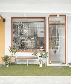 an outside view of a store front with plants in the window and potted grass on the lawn