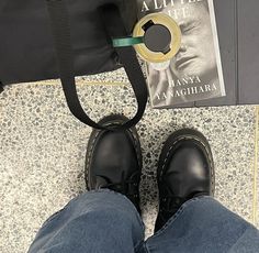 a pair of black shoes sitting next to a book and bag on the ground near a person's feet