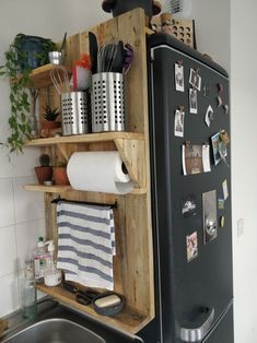 a kitchen with a black refrigerator and wooden shelves filled with utensils, cups, and other items