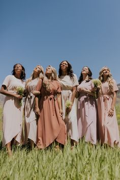 the bridesmaids are standing in a field with their heads together and looking up at the sky