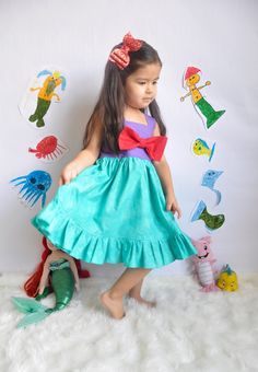 "This Princess Ariel inspired dress is one of my favorites! This bright colored dress is perfect for a themed Birthday Party, dress up, or a trip to that famous Park! The skirt has a wavy water effect. A pretty ruffle accents the hem. The fully lined bodice has an elastic back for a comfortable fit. A bright red bow highlights the front of the bodice. 100% cotton. Machine wash cold. Tumble dry low. Approximate Measurements: 3-6 mo. 12-16 lbs. 6-9 mo. 16-20.5 lbs. 9-12 mo.20.5-24.5 lbs. chest 12- Green Sleeveless Princess Dress, Cute Sleeveless Princess Dress For Playtime, Pink Fun Dress For Costume Party, Fun Pink Dress For Costume Party, Playful Princess Dress For Summer Costume Party, Playful Summer Princess Dress For Costume Party, Playful Purple Princess Dress For Summer, Playful Purple Dress For Dress-up Occasions, Blue Mermaid Dress For Summer Dress-up