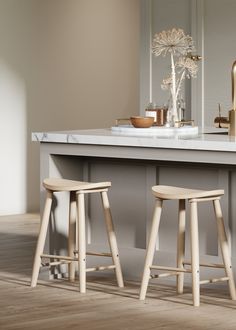 two wooden stools sitting in front of a counter top with a vase on it