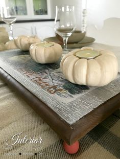 some pumpkins are sitting on top of a table with wine glasses and plates in the background