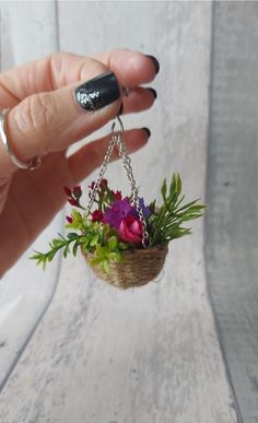 a hand holding a small flower pot with flowers hanging from it's chain,