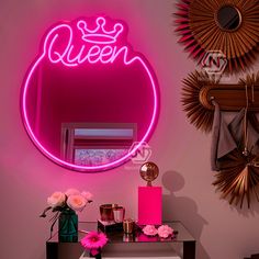 a pink neon sign that says queen on the wall next to a mirror and vase with flowers