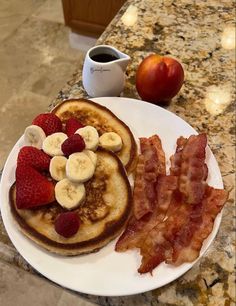 pancakes with bacon, bananas and strawberries are on a plate next to an apple