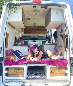 a woman laying on top of a bed in the back of a white van with open doors