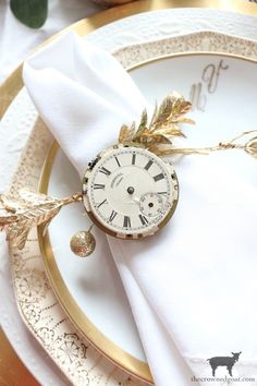 a white plate topped with a gold clock on it's side next to a napkin