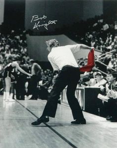 a man holding a tennis racquet on top of a hard wood floor in front of an audience