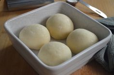 three doughnuts in a white bowl on a wooden table next to a knife