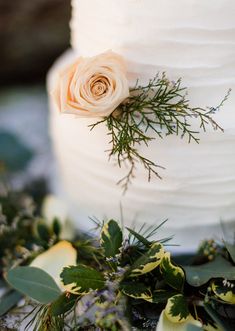 a close up of a white cake with flowers on it and greenery around the edges