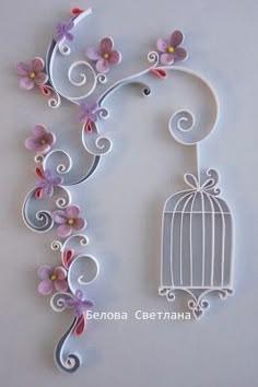 a white birdcage with pink flowers hanging from it's side next to a wall